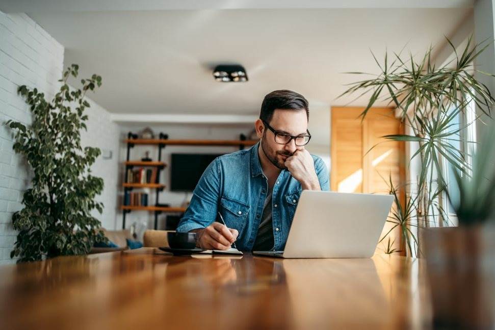 Man taking notes from laptop at his desk