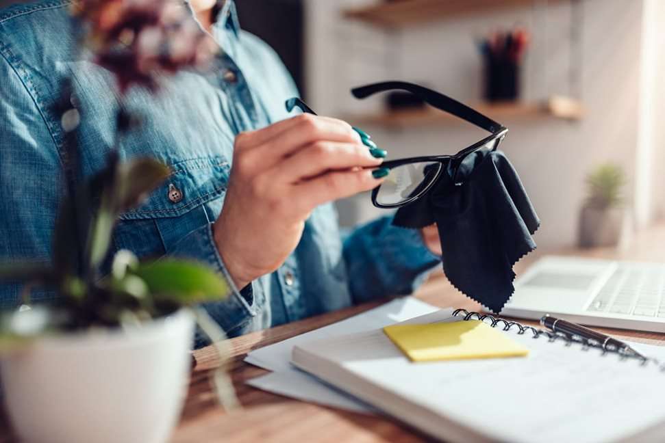 Woman at desk cleaning glasses with cloth