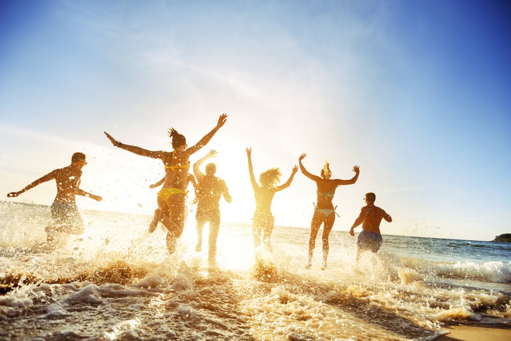 Friends on holiday running into water at beach