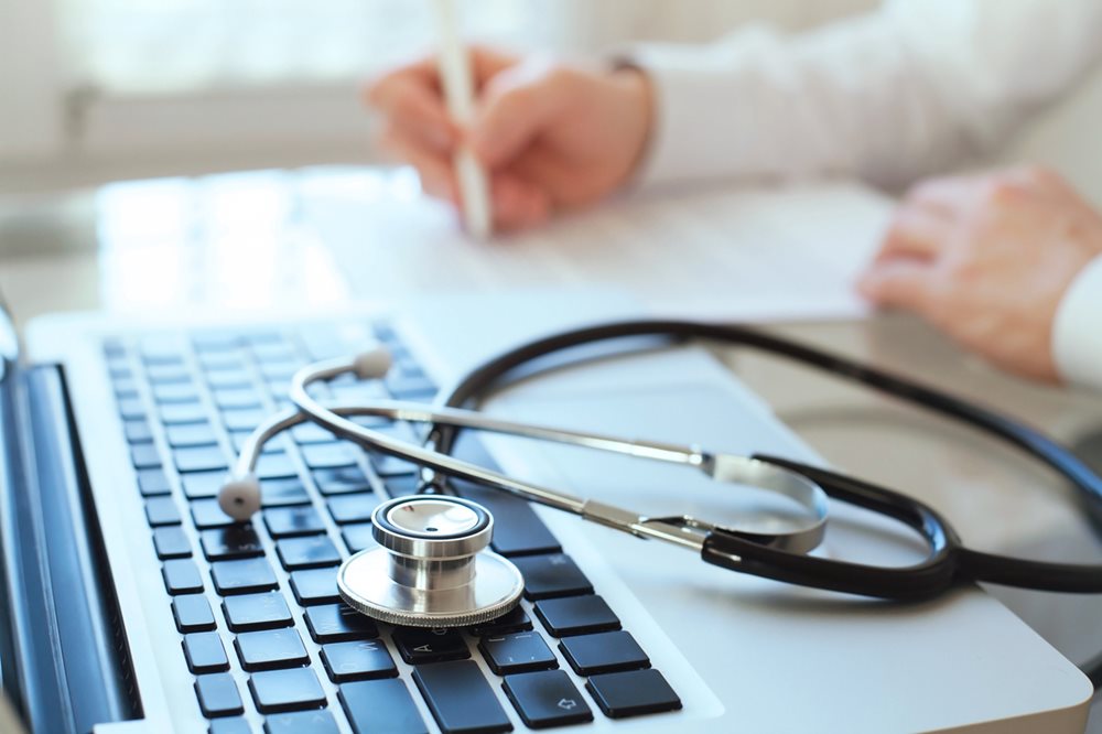 Doctor with stethoscope writing at computer 