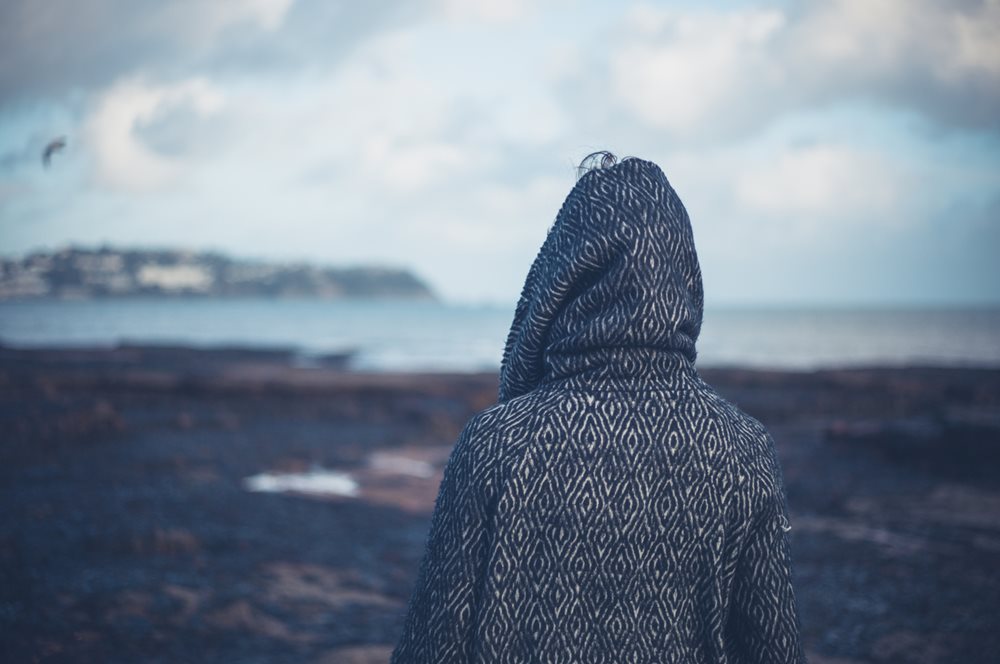Woman in hoodie staring out to sea in winter