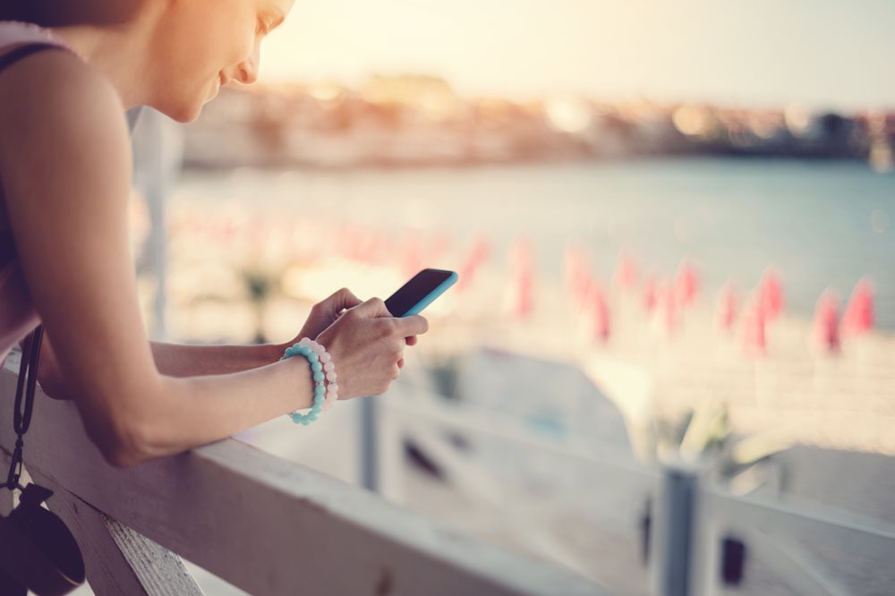 Woman on her phone overlooking beach in sunshine