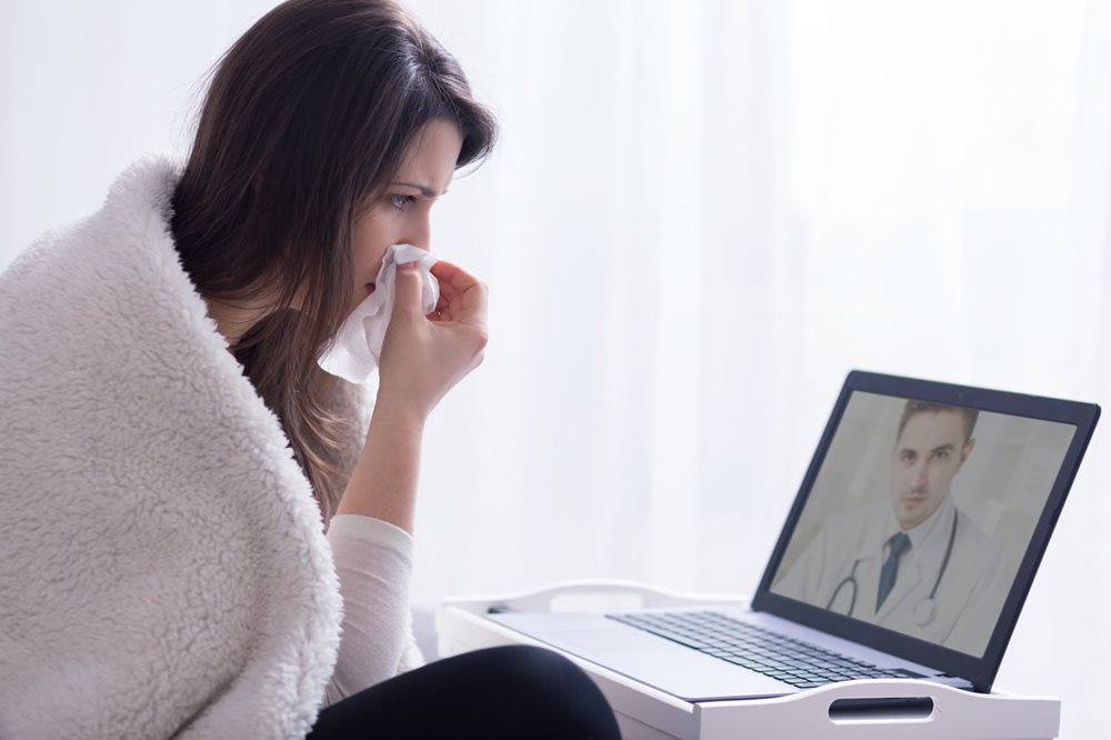 Woman with cold accessing digital doctor on laptop