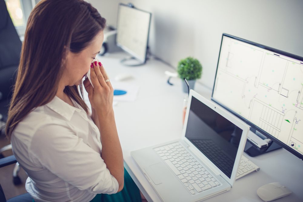 Woman blowing her nose at her office desk